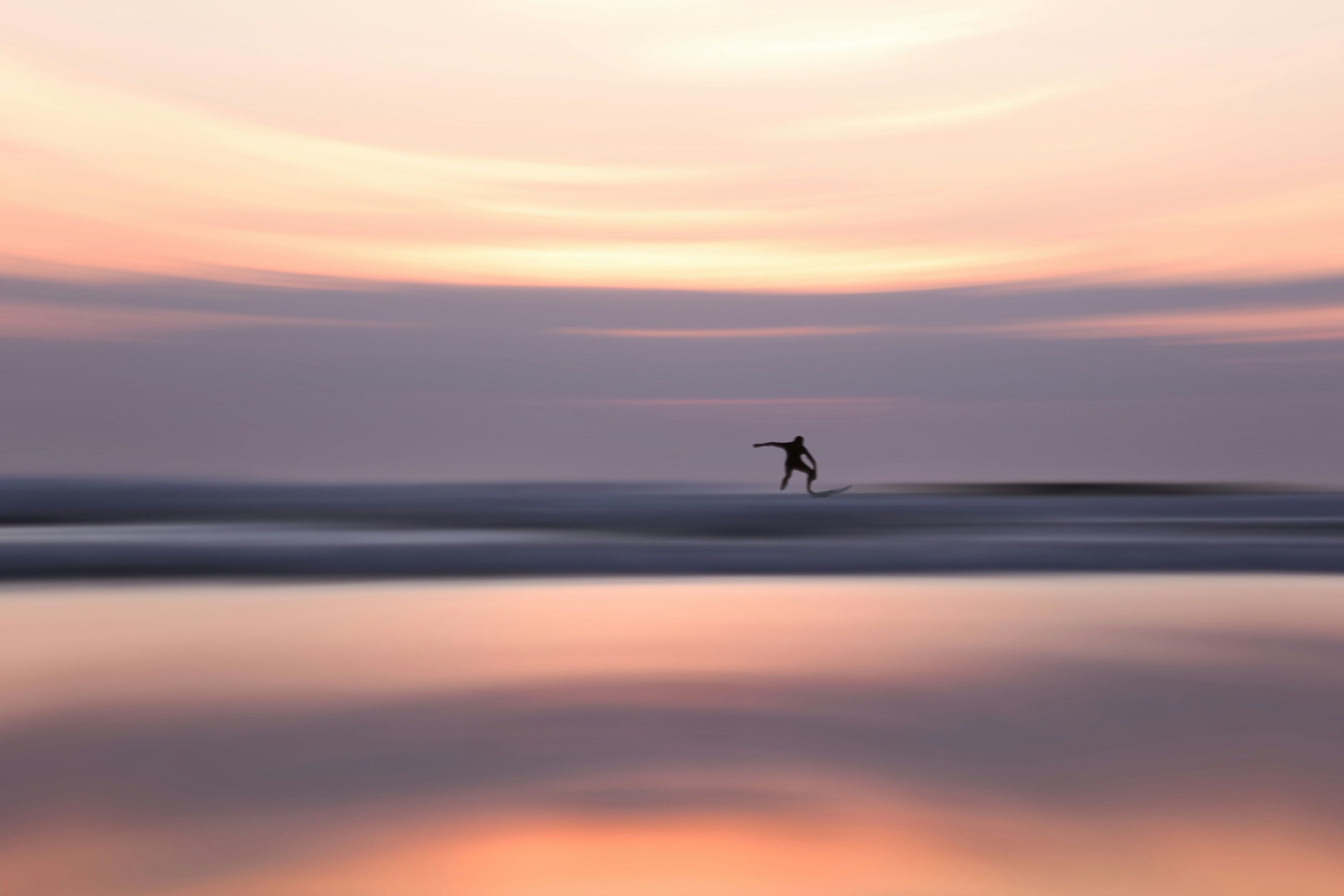 A person surfing on a calm body of water during sunset.