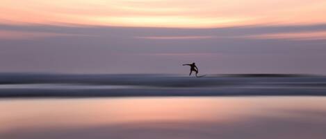 A person surfing on a calm body of water during sunset.