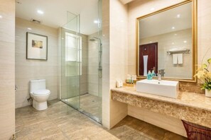 Un baño moderno con ducha de vidrio, inodoro blanco y encimera de mármol con lavabo y espejo.