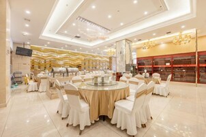 Un salón de banquetes con mesas redondas, sillas blancas y un candelabro.