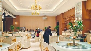 A hotel lobby with round tables, chairs with gold sashes, and a chandelier. - Jinyuan Hotel (Hui County)