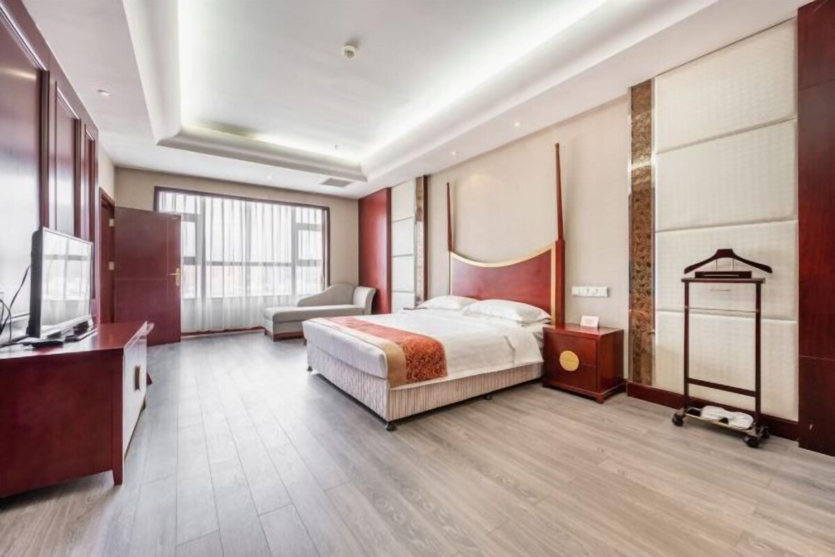 Habitación de hotel con cama, mesita de noche, televisor, armario y ventana con cortinas.