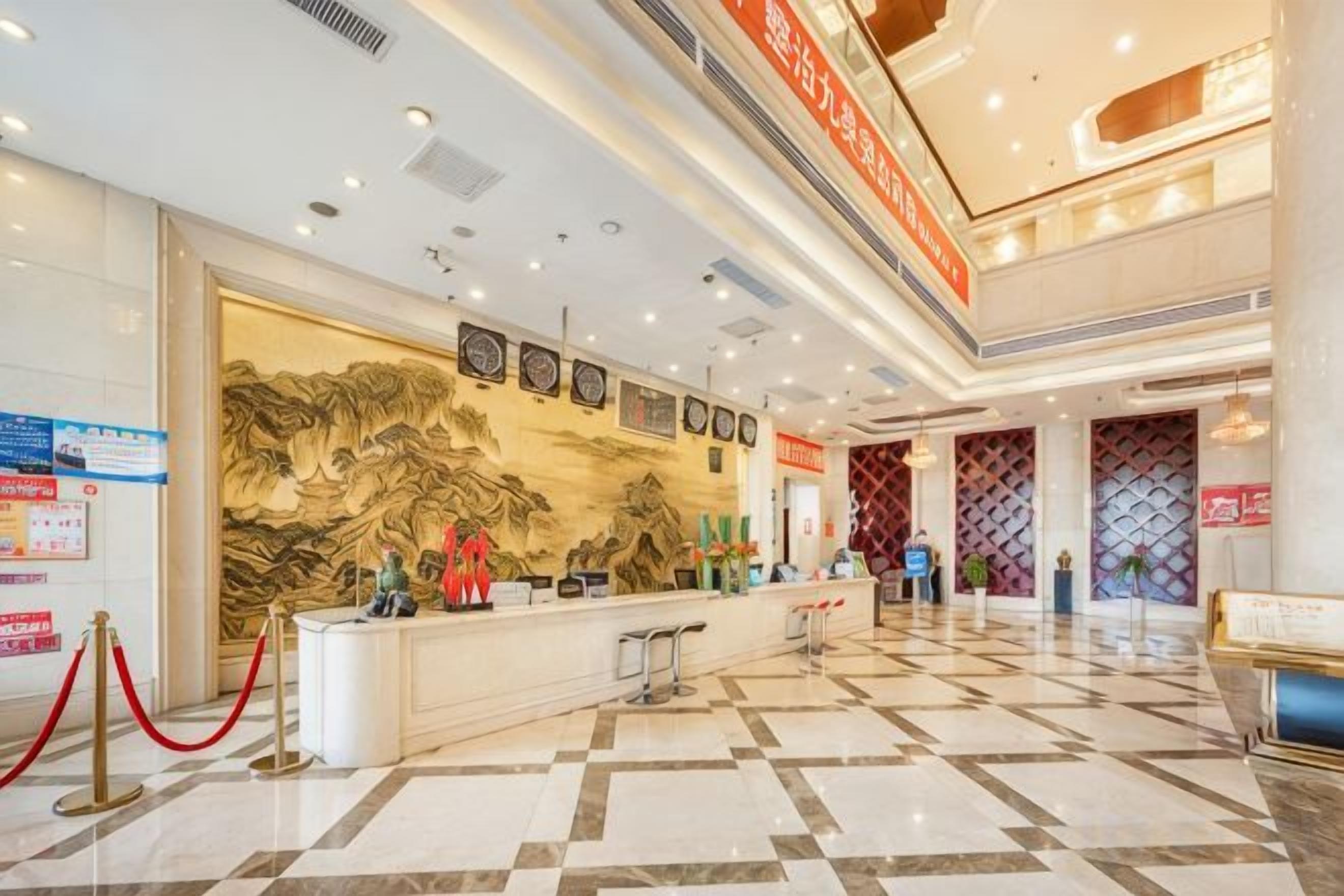 A hotel lobby with a reception desk, a large decorative wall, and a check-in counter.