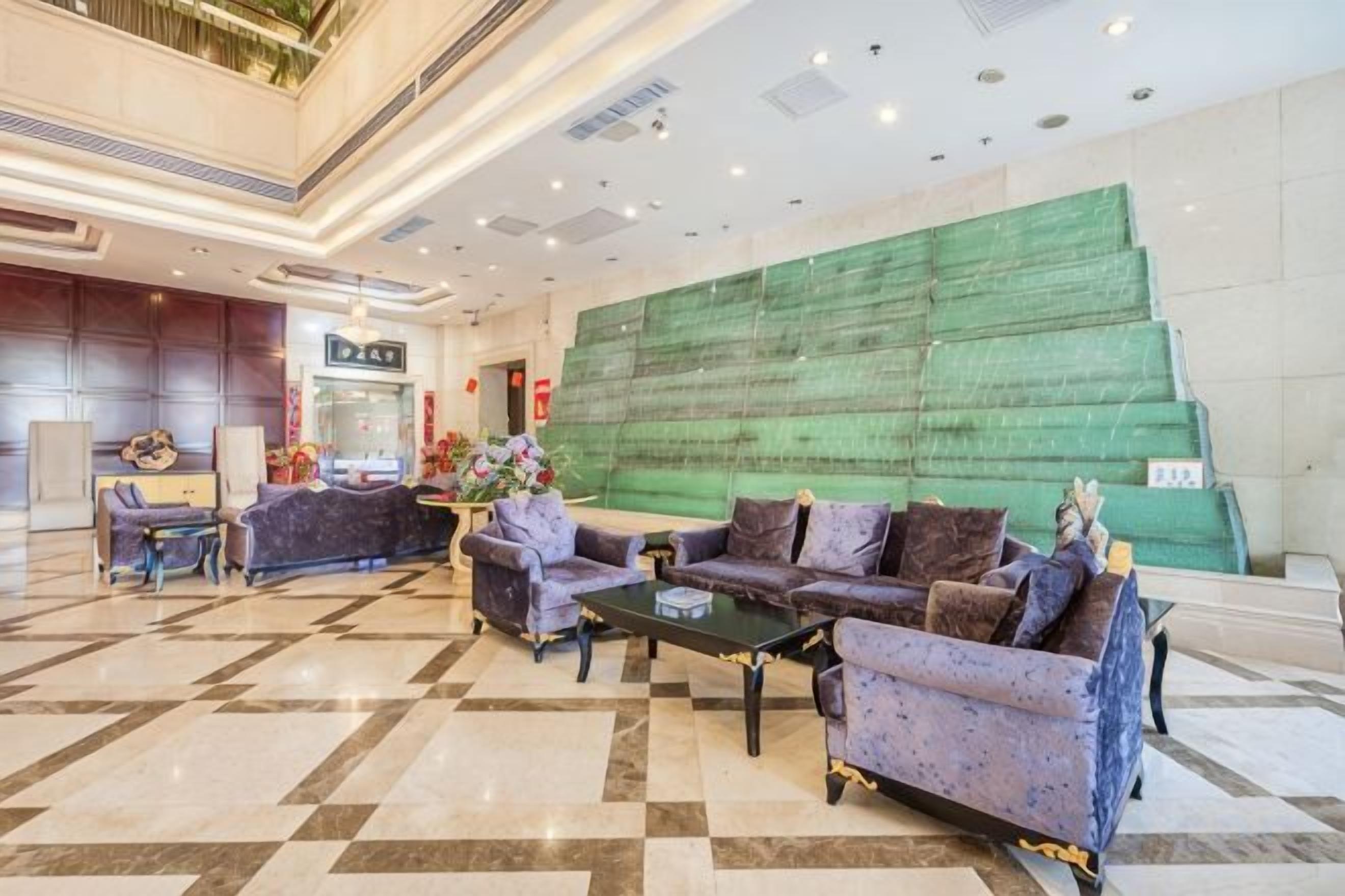 A hotel lobby with a check-in counter, seating area with sofas and a coffee table, and a large green wall.