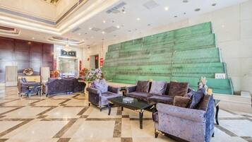 A hotel lobby with a check-in counter, seating area with sofas and a coffee table, and a large green wall.