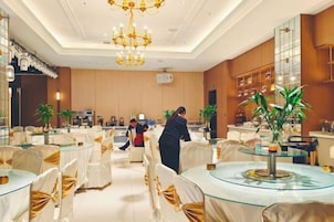 A hotel lobby with round tables, chairs, and a chandelier.
