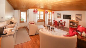 A cozy living room with a sofa, a dining area with a table and chairs, a kitchen with a sink and stove, and a bookshelf.