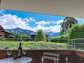 Una terraza con una mesa, copas de vino y una botella, con vistas a un paisaje montañoso.