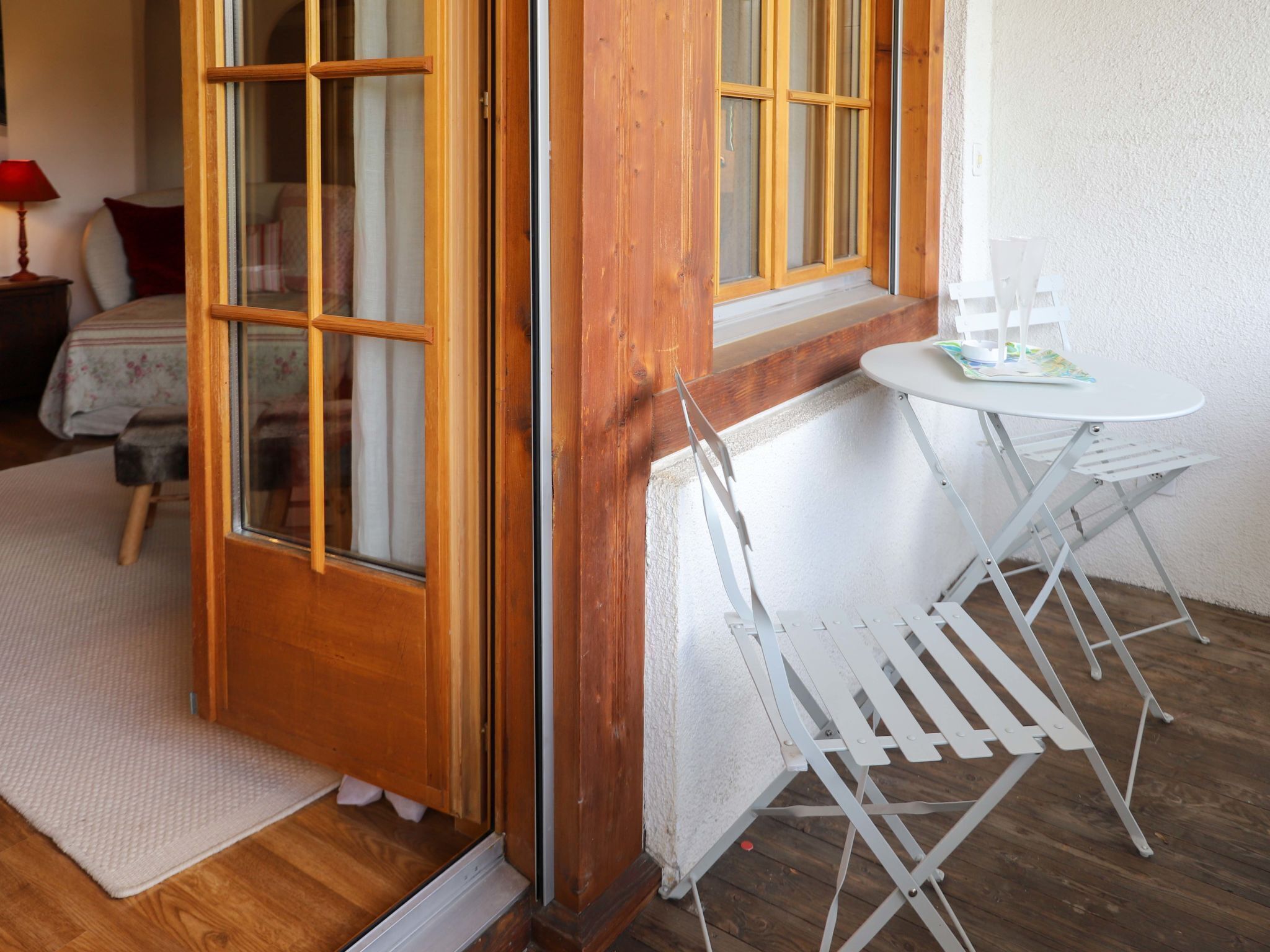 A room with a wooden door, a small white table with chairs, and a bed with a floral bedspread.