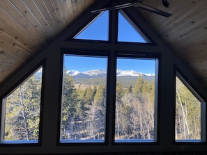 Une pièce dotée d’un plafond en pente et de grandes fenêtres offrant une vue sur des montagnes enneigées et un paysage boisé.