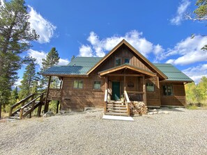 Un chalet en bois avec un toit vert, un porche et une allée gravillonnée.