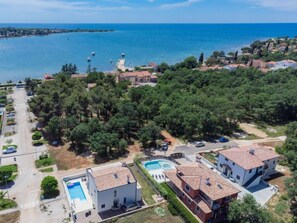 An aerial view of a coastal residential area with houses, a swimming pool, and a clear view of the sea.