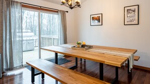 Un comedor con una mesa de madera y bancos, una araña y dos cuadros en la pared.