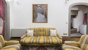 A living room with a sofa, patterned cushions, a framed picture on the wall, and a patterned rug. - Velluti apartment for rent by Mmega (Florence)