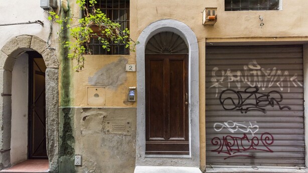 A building with a closed garage door, a wooden door, and a number '2' sign. - Velluti apartment for rent by Mmega (Florence)