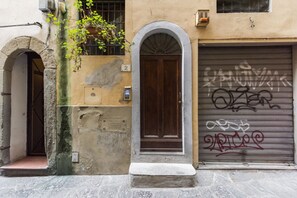 A building with a closed garage door, a wooden door, and a number '2' sign. - Velluti apartment for rent by Mmega (Florence)