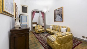 A living room with a sofa set, a small table, and a vase. There is a door leading to another room. - Velluti apartment for rent by Mmega (Florence)