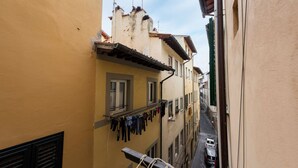 A narrow street with buildings on either side, a balcony with clothes hanging, and a car parked on the street. - Velluti apartment for rent by Mmega (Florence)