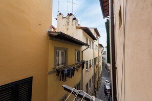A narrow street with buildings on either side, a balcony with clothes hanging, and a car parked on the street.