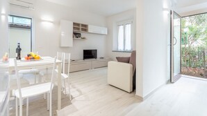 Ein modernes Wohnzimmer mit Essbereich, einer Couch, einem Fernseher und einer Küchenzeile.