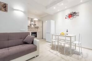 A modern living space with a sofa, dining table, chairs, a kitchen area, and artwork on the walls.