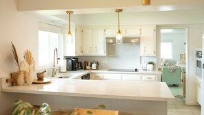 A modern kitchen with white cabinetry, a large island, pendant lights, and a view into the living area.