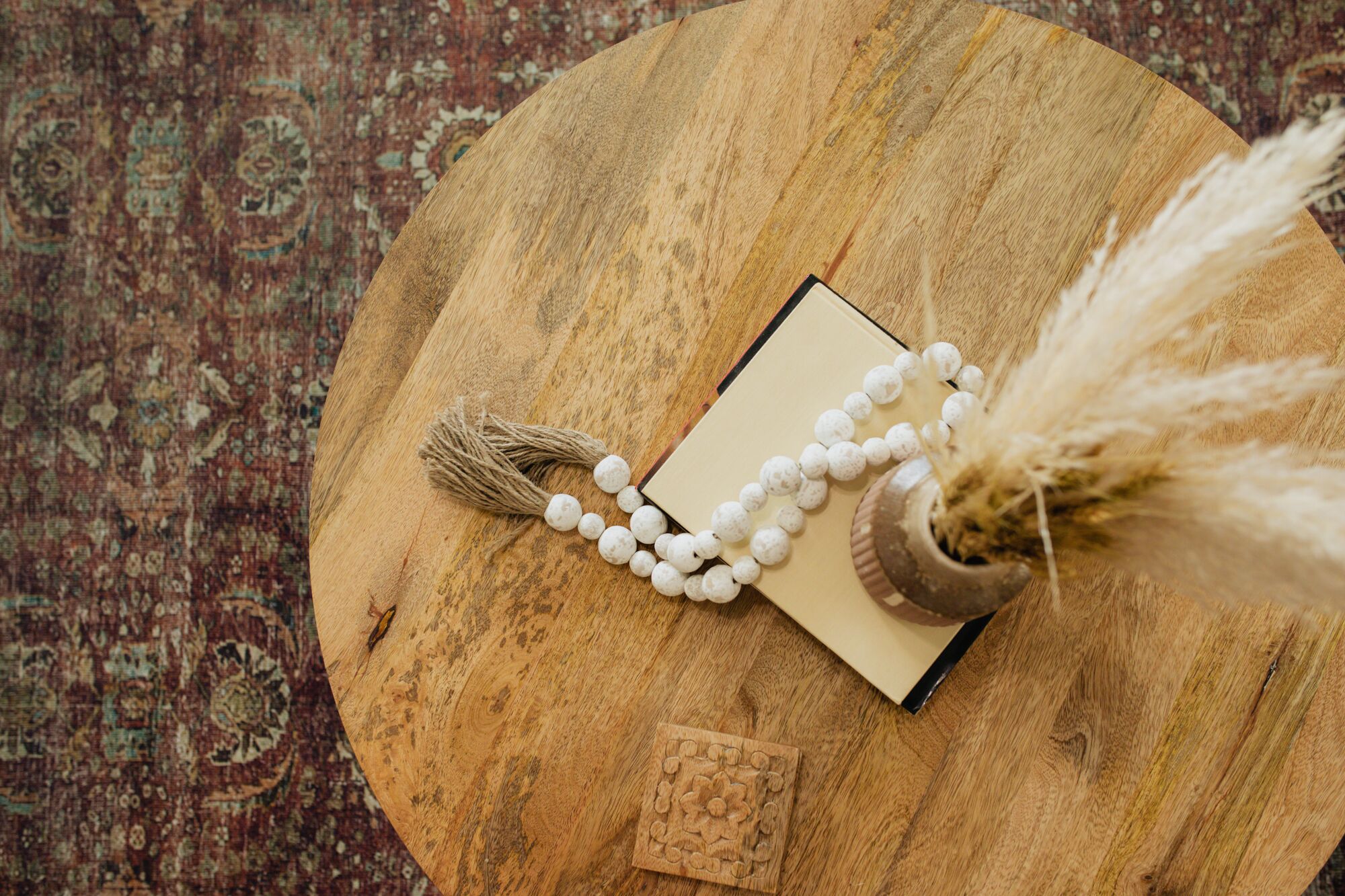 Een ronde houten tafel met een boek, een kralenketting en een klein decoratief object.