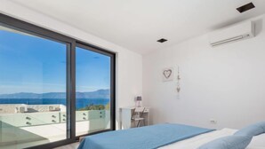 A bedroom with a large window, a bed with blue bedding, and a view of the sea and mountains. - Apartment Albi by Interhome (Rijeka)