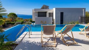 A modern pool area with a clear view of the sea, a contemporary building, and two wooden lounge chairs. - Apartment Albi by Interhome (Rijeka)