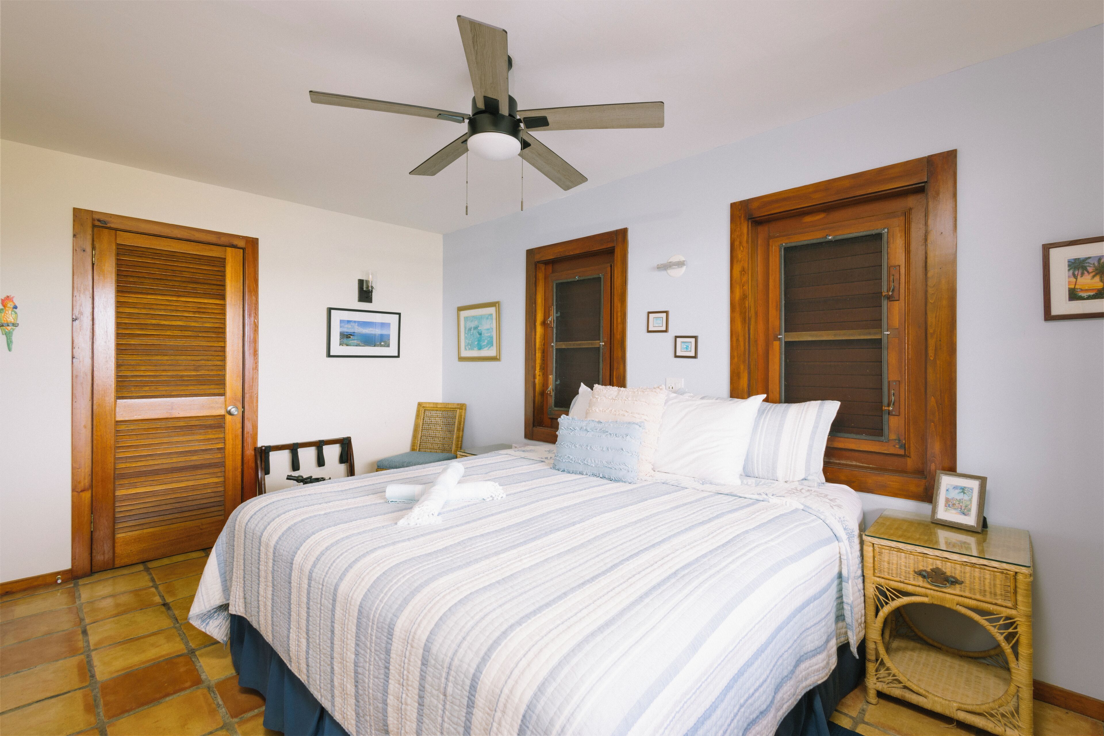 A bedroom with a bed, wooden doors, a ceiling fan, and a wicker nightstand.