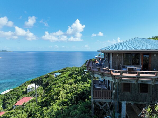 A wooden structure with a blue roof overlooking a coastal area with lush greenery and a view of the ocean.