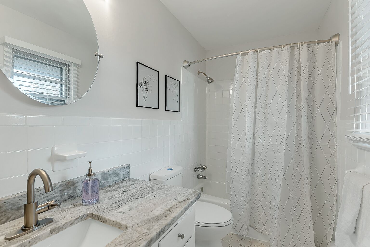 Ein Badezimmer mit Marmorwaschbecken, Toilette, Dusche mit einem diamantmuster-Vorhang und einem Fenster mit Jalousien.