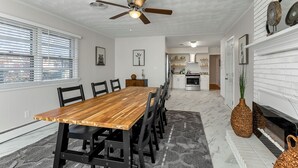 A dining area with a wooden table and chairs, a ceiling fan, and a kitchen in the background.