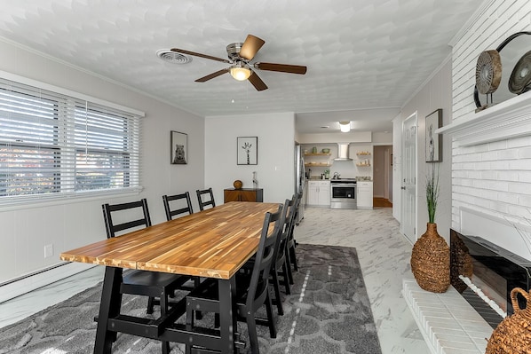 A dining area with a wooden table and chairs, a ceiling fan, and a kitchen in the background.