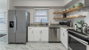A modern kitchen with a refrigerator, dishwasher, microwave, oven, and a window with blinds.