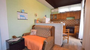 A cozy room with a sofa, a small table, and a kitchen area with wooden cabinets and a stove. - Apartment Potnar M with balcony (Malinska)
