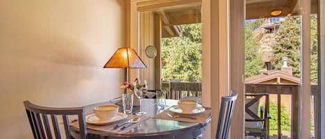 A dining area with a table set for two, a lamp, and a view of the outdoors.