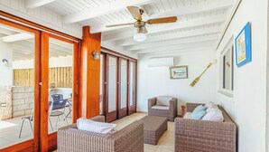 A spacious room with wicker furniture, a ceiling fan, and a view through a glass door to an outdoor area with chairs.