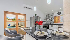 A modern kitchen with a central island, a dining area with chairs, and a view of a swimming pool. - Breathtaking Views 2BR3BA Private Pool Large Space (Noord)