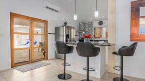 A modern kitchen with a central island, two bar stools, and a view into the dining area. - Breathtaking Views 2BR3BA Private Pool Large Space (Noord)