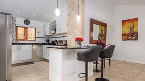 A modern kitchen with a central island, bar stools, a clock, and artwork on the walls. - Breathtaking Views 2BR3BA Private Pool Large Space (Noord)