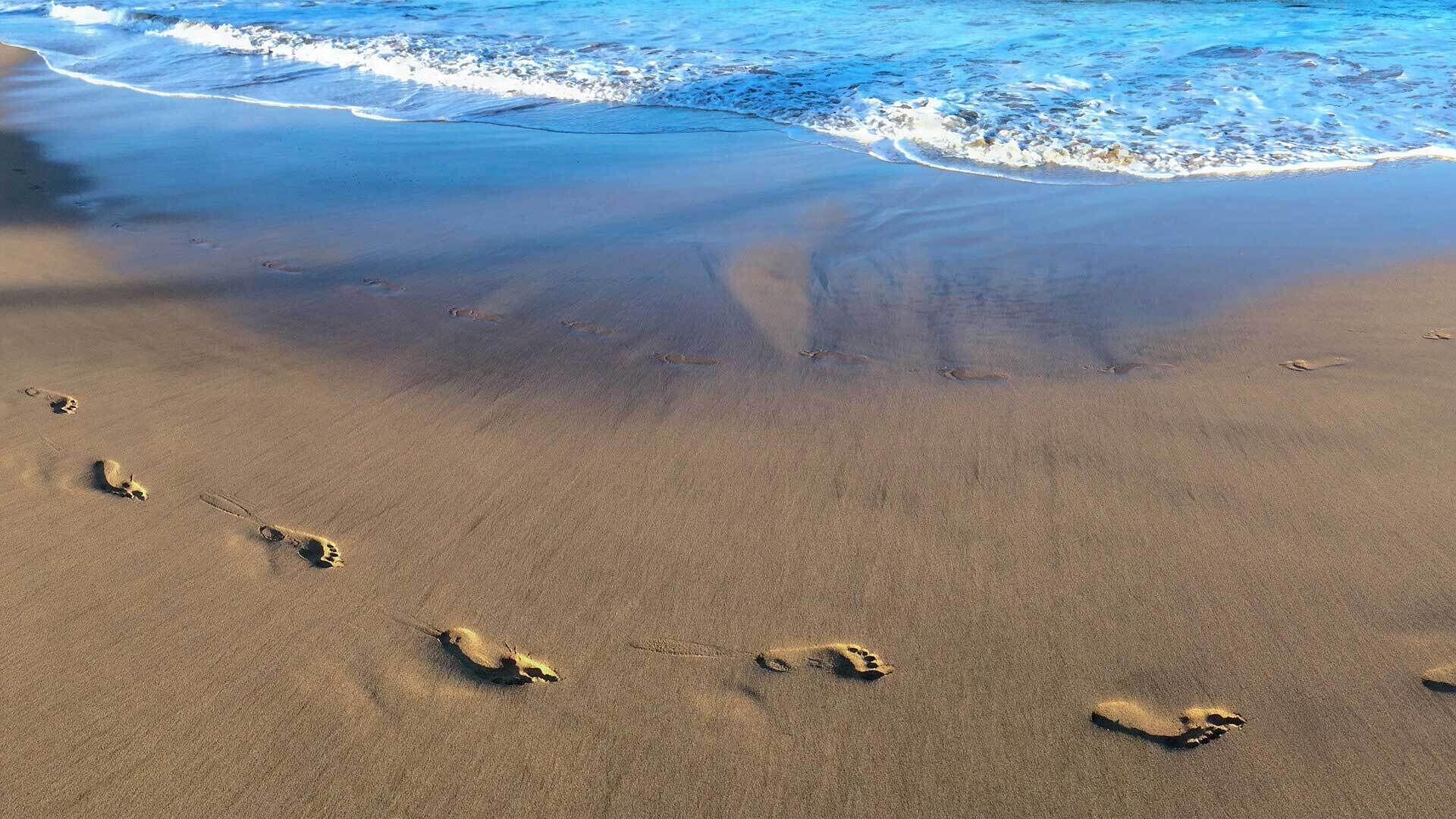 A sandy beach with footprints leading towards the ocean.