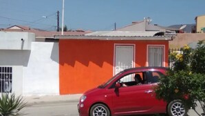 A red car parked in front of a building with a white and orange facade. - Studio independiente (Ensenada)