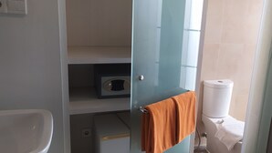 Une salle de bain avec une porte en verre, des toilettes blanches et une étagère sur laquelle se trouve une radio.