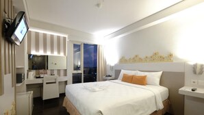 Une chambre d’hôtel avec un grand lit, un bureau avec une chaise, une télévision et une fenêtre avec des rideaux.