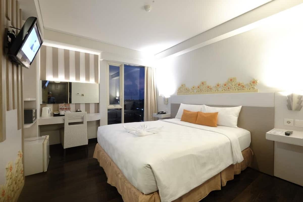 A hotel room with a large bed, a desk with a chair, a television, and a window with curtains.