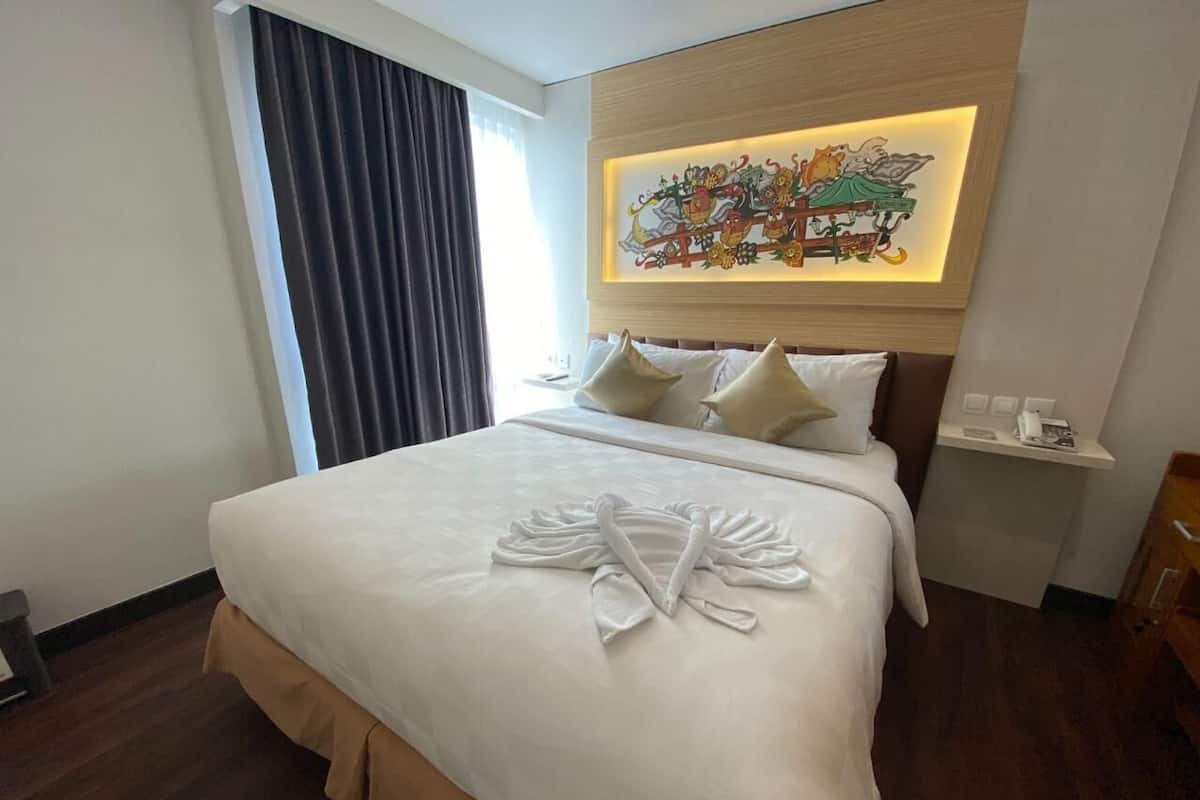 A hotel room with a neatly made bed, a headboard with a decorative light, and a wall-mounted artwork.
