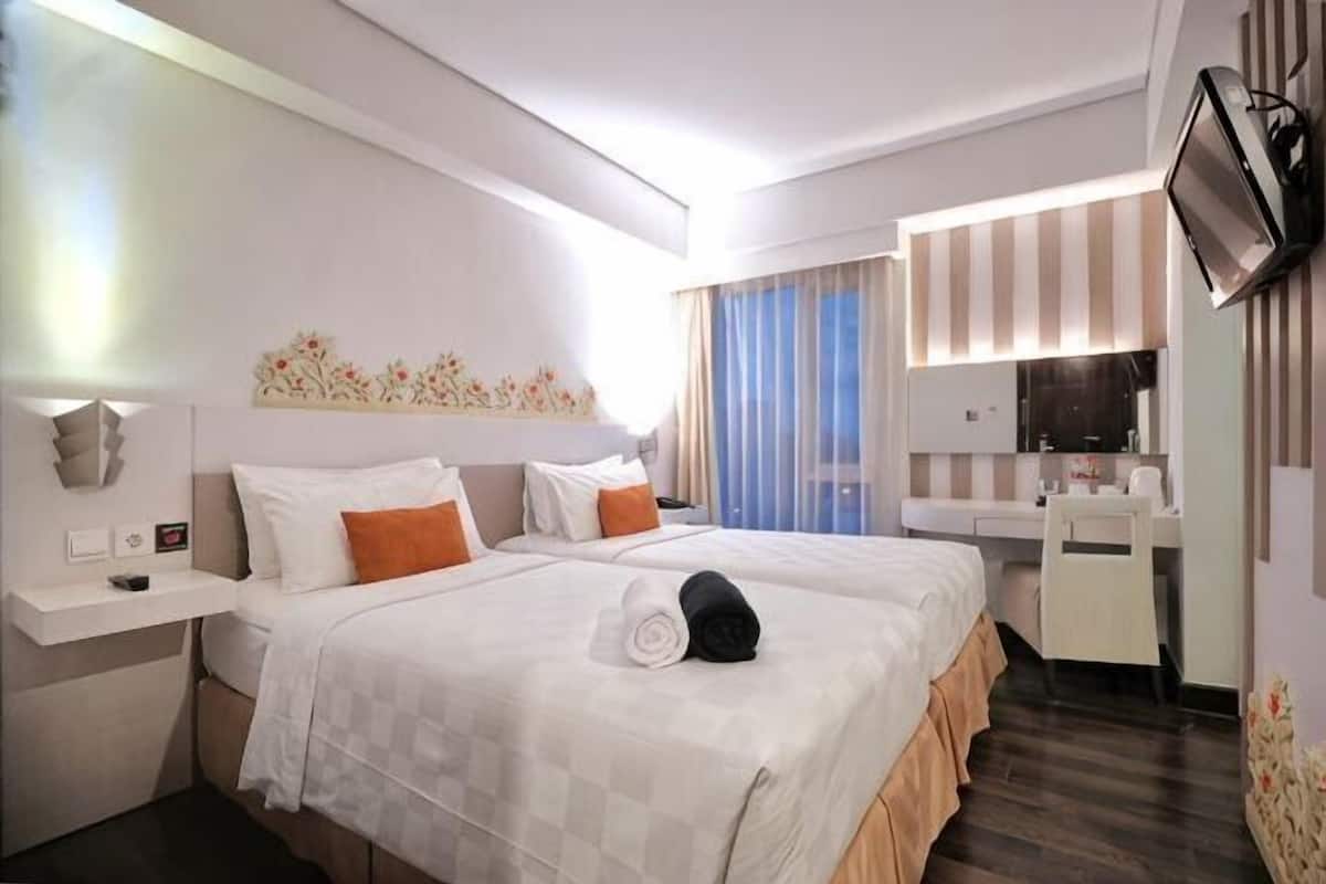 A hotel room with a bed, a desk, a chair, a TV, and a window with curtains.