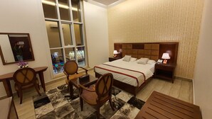 A hotel room with a large bed, two bedside tables with lamps, a desk with a chair, and a large window with a view of the city. - Pearl Of Vision Hotel (Jeddah)