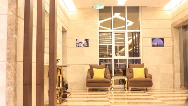 A lobby with two armchairs, a checkered floor, and a large window with a cityscape view. - Pearl Of Vision Hotel (Jeddah)